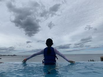 Rear view of girl swimming in sea against sky