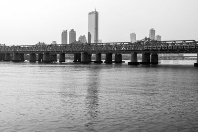 Bridge over river by buildings against clear sky