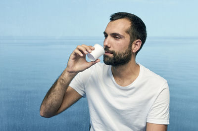 Man drinking coffee against glass with sea in background