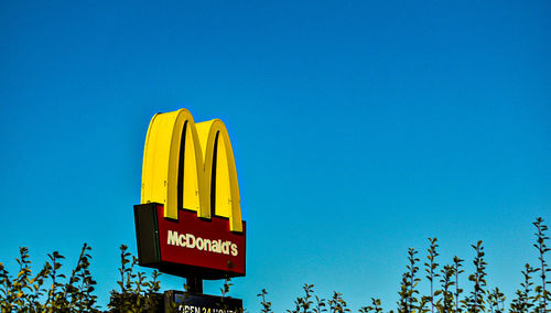 Low angle view of yellow sign against clear blue sky