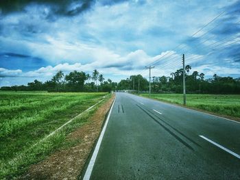 Road passing through field against cloudy sky