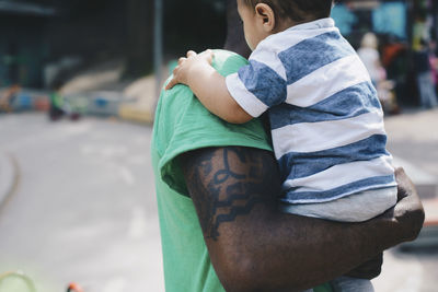 Father with tattoo carrying son at park