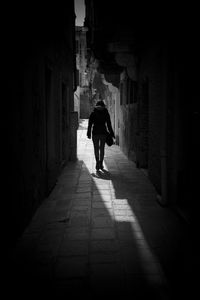 Full length rear view of woman walking in alley amidst buildings