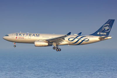 Airplane flying over water against clear blue sky