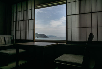 Empty chairs and tables against sky seen through window