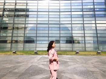 Rear view of young woman standing against glass building