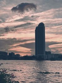 Sea by modern buildings against sky during sunset