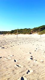 Footprints on sand at beach against clear blue sky