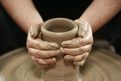 Cropped hands of person working on pottery wheel in mud