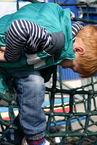 Boy wearing jacket sitting on jungle gym at playground