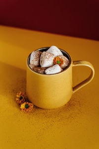 Still life of a yellow mug of hot cocoa with marshmallows.