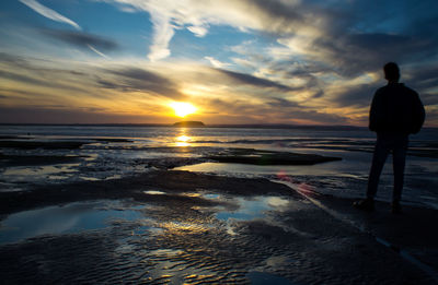 Rear view of silhouette man standing on beach during sunset