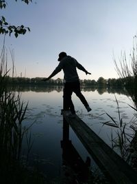 Rear view of silhouette man standing on pier over lake against sky