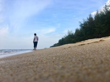 Surface level view of man walking at beach against blue sky