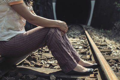 Low section of woman sitting on railroad track