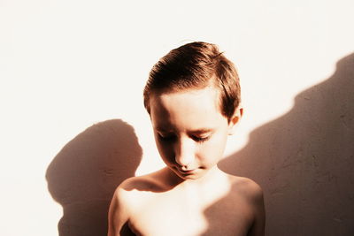 Sad shirtless boy against wall during sunny day