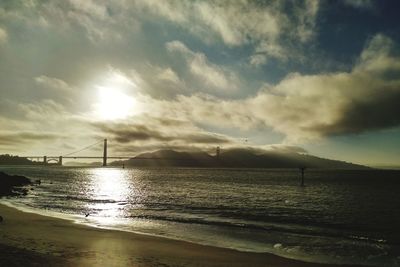 View of suspension bridge over sea against cloudy sky