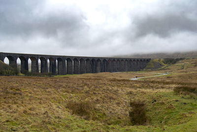 Arch bridge over field against sky