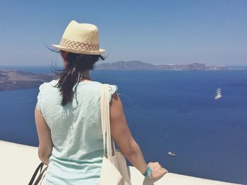 Rear view of woman standing by retaining wall against sea at santorini