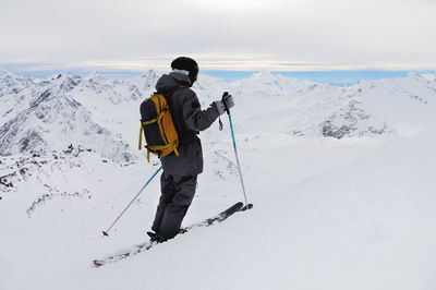 Side view of an athletic skier in a helmet and goggles with a backpack, standing on skis, holding