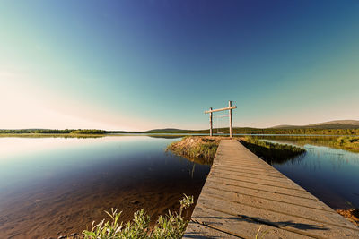 Pier over lake against clear blue sky