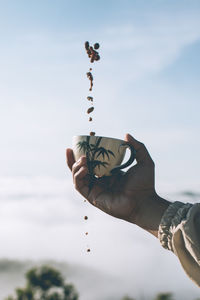 Midsection of person holding coffee cup against sky