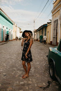 Full length portrait of woman standing on street amidst buildings in city