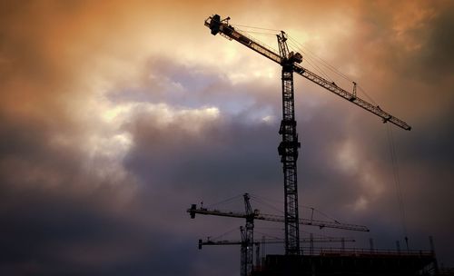 Low angle view of cranes at construction site against sky