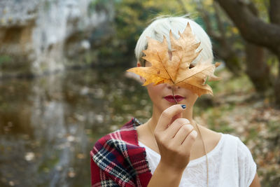 Close-up of young woman holding autumn leaf against tree