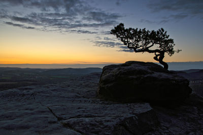 Silhouette rocks on land against sky during sunset