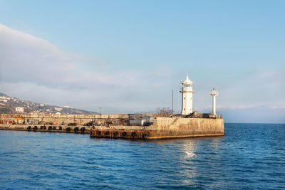 Lighthouse by sea against clear sky