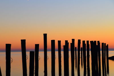 Wooden posts in sea against clear sky during sunset