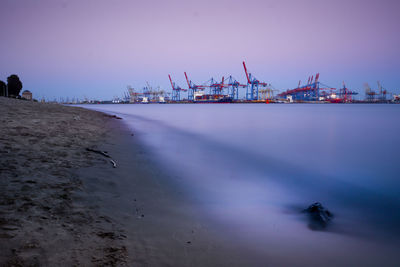 Oil drills in sea against sky during sunset