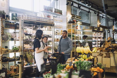 Customers discussing with female retail clerk at convenience store