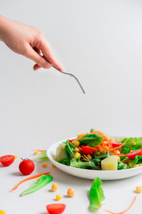 Cropped image of hand holding strawberry over white background