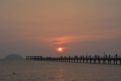 Silhouette wooden posts in sea against orange sky