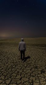 Rear view of man standing on cracked field against star field