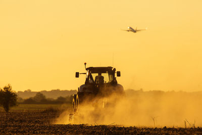 Airplane flying over land against sky during sunset