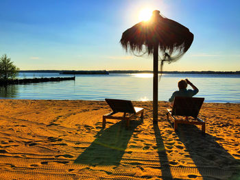 Rear view of man sitting on lounge chair at sandy beach