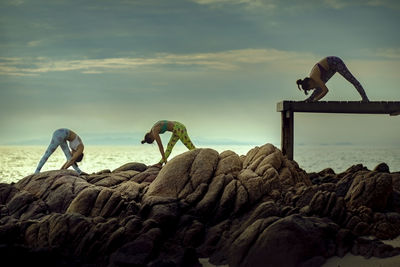 People on rocks by sea against sky