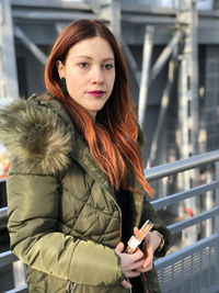 Woman looking away while holding mobile phone against railing