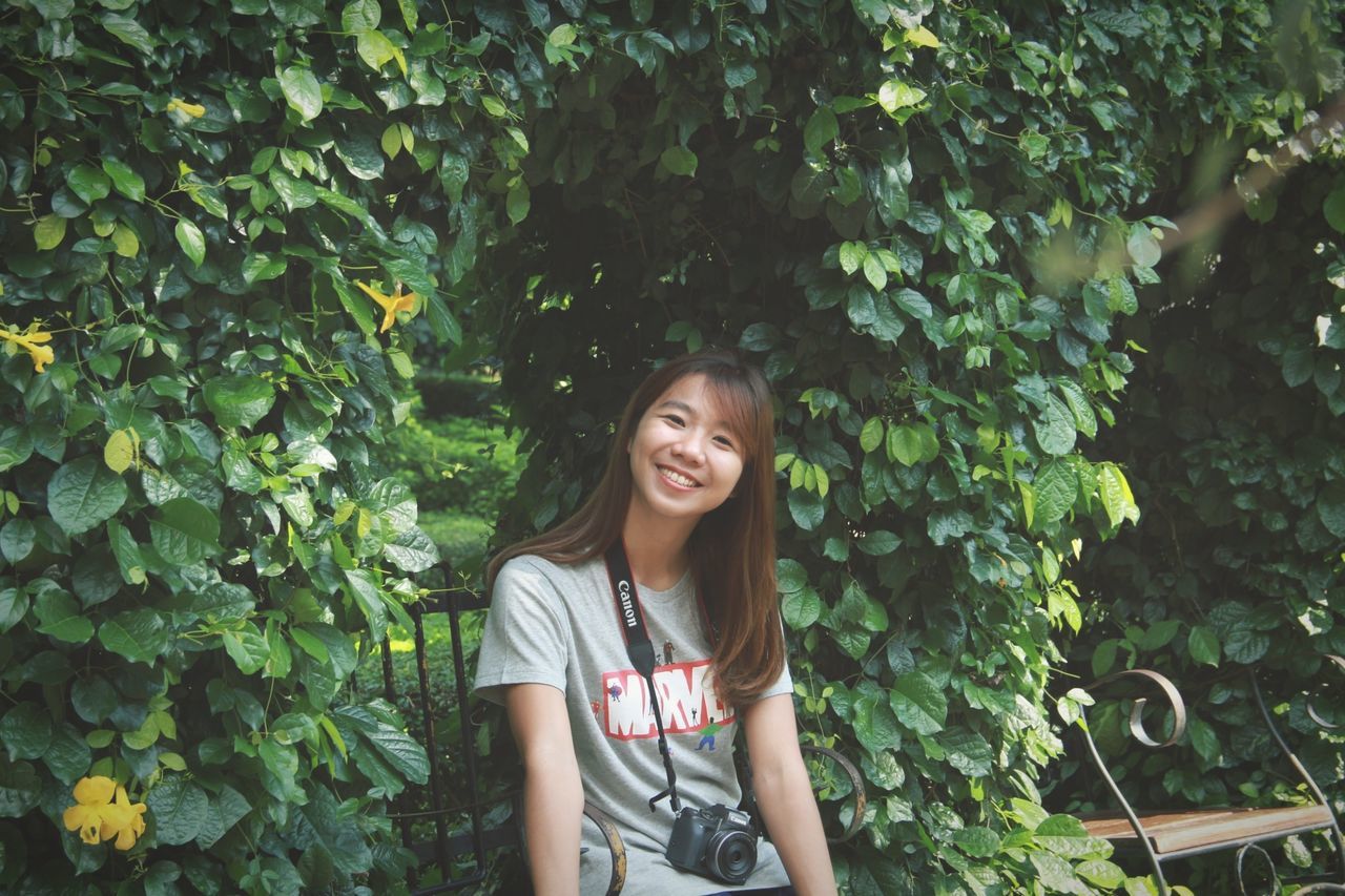 one person, smiling, portrait, real people, front view, standing, young adult, plant, casual clothing, young women, looking at camera, lifestyles, happiness, leisure activity, tree, waist up, growth, day, emotion, hairstyle, beautiful woman, hair, outdoors