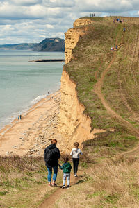 Rear view of men walking on shore by sea against sky