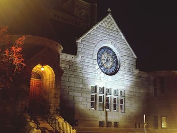 Low angle view of illuminated clock amidst buildings at night