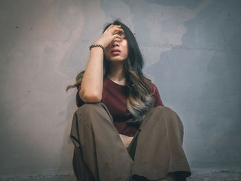 Young woman looking away while sitting against wall