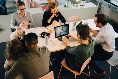 High angle view of business people discussing while sitting with boy and dog at desk in creative office