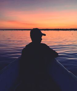 Silhouette man sitting in boat on sea against sky during sunset