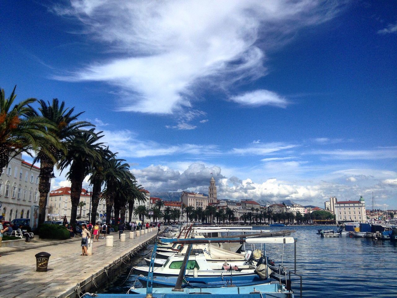 building exterior, sky, architecture, built structure, water, palm tree, tree, sea, cloud - sky, blue, cloud, city, incidental people, large group of people, day, beach, city life, tourist resort, sunlight