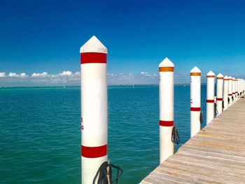 Wooden posts on pier over sea against blue sky