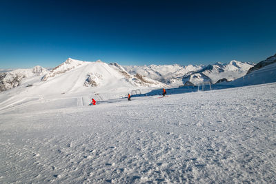 People skiing on snowcapped mountains against clear blue sky
